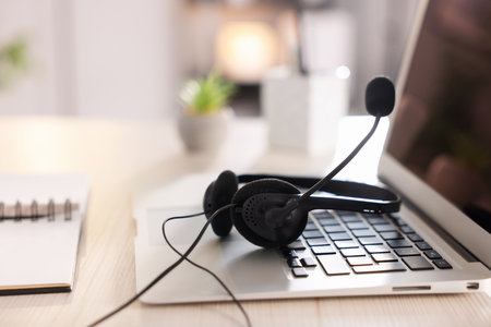 Headset with microphone and laptop on white wooden desk in office, closeup. Space for textの写真素材