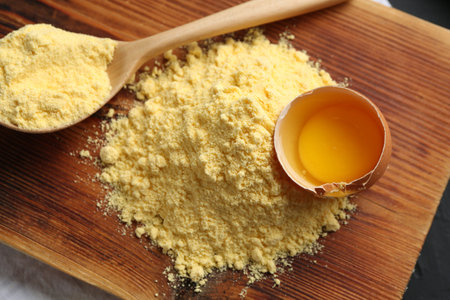 Pile of corn flour, spoon and broken egg on table, top view
