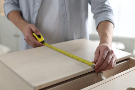Man measuring wooden cabinet with tape indoors, closeupの写真素材