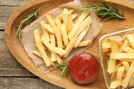 Tasty french fries served with ketchup and rosemary on wooden table, top view
