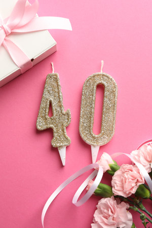 40th birthday. Number shaped candles, gift and flowers on pink background, flat layの写真素材
