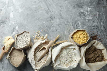 Different types of flour in bags on grey textured table, flat lay. Space for textの写真素材