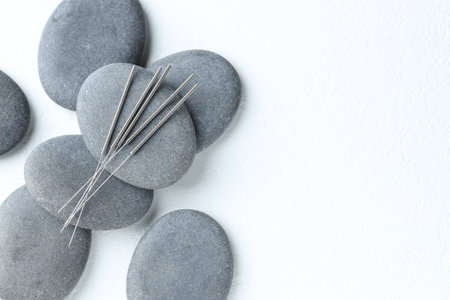 Acupuncture needles and spa stones on white background, flat lay. Space for textの写真素材
