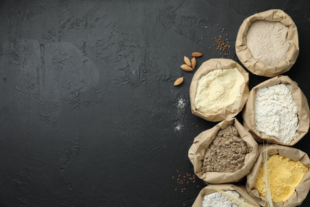 Different types of flour in paper bags on black table, flat lay. Space for textの写真素材