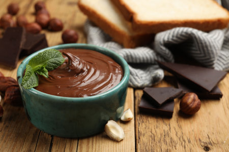 Tasty hazelnut spread with mint, chocolate pieces and nuts on wooden table, closeupの写真素材