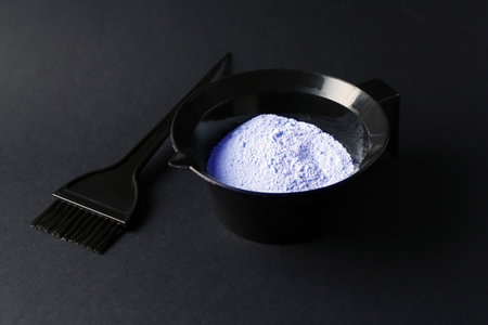 Bowl with hair bleaching powder and brush on black background, closeupの写真素材