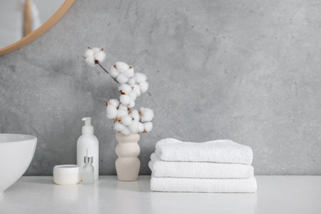 Stack of clean towels, cosmetic products and cotton flowers on vanity in bathroomの写真素材