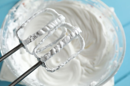 Hand mixer with whisks and bowl of whipped cream on light blue table, above viewの写真素材