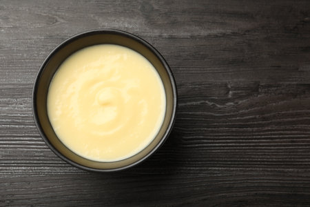 Tasty vanilla pudding in bowl on wooden table, top view. Space for textの写真素材