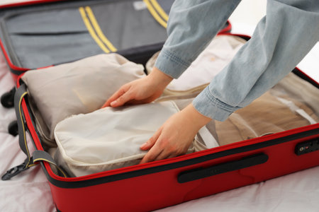Woman putting packing cube into suitcase indoors, closeupの写真素材