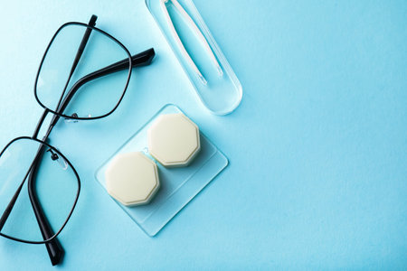 Contact lens case, glasses and tweezers on light blue background, flat lay. Space for text