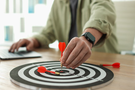 Man with dart aiming at dartboard while working on laptop indoors, closeupの写真素材