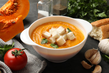 Tasty pumpkin cream soup with croutons and parsley in bowl among other products on dark table, closeupの写真素材