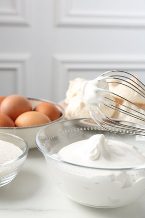 Whisk with whipped cream and other ingredients on light table, closeup. Cooking meringue cookiesの写真素材