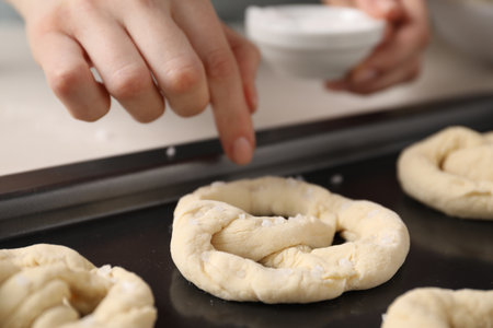 Woman putting salt onto raw pretzels at white table, closeupの写真素材