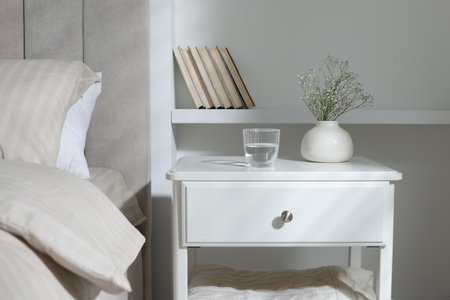 Bedside table with flowers in vase and glass of water near bed indoorsの写真素材