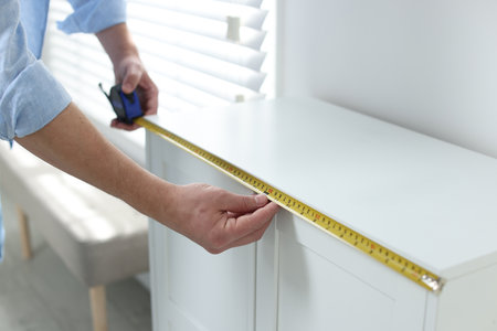 Man measuring white cabinet with tape indoors, closeupの写真素材