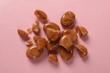 Many tasty caramel candies on light pink background, flat layの写真素材
