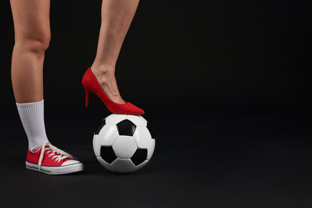 Woman in high heeled shoe and sneaker with soccer ball on dark background, closeup. Space for textの写真素材