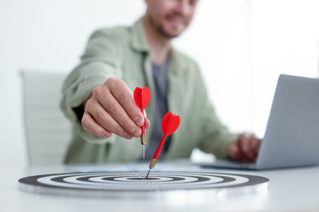 Man with dart aiming at dartboard while working indoors, closeupの写真素材