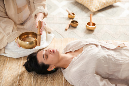 Woman undergoing singing bowl therapy lying on floor indoorsの写真素材