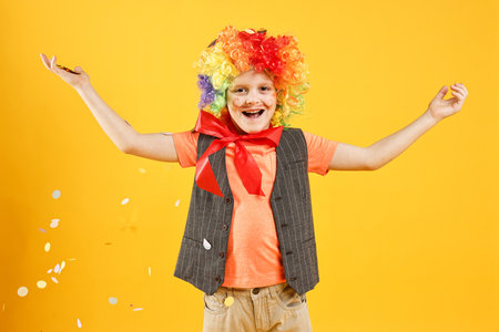 Happy little boy dressed like clown and flying confetti on orange background. Surprise partyの写真素材