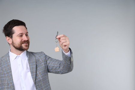 Real estate agent holding key with house shaped keychain on light grey background, space for textの写真素材