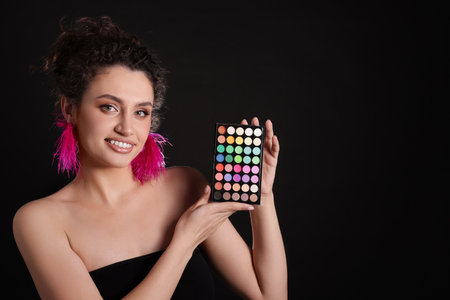 Smiling woman with bright eyeshadow palette on black background. Space for textの写真素材