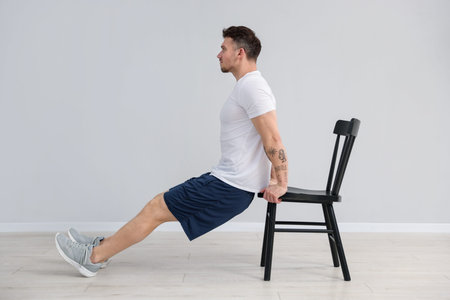 Handsome man exercising with chair at home
