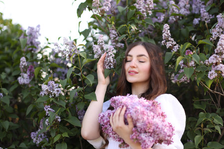 Smiling woman among lilac flowers and leaves outdoorsの写真素材
