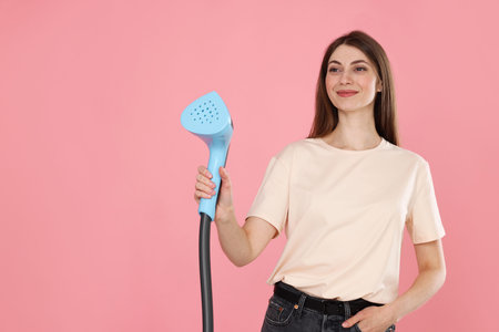 Woman with clothes steamer on pink background. Space for text
