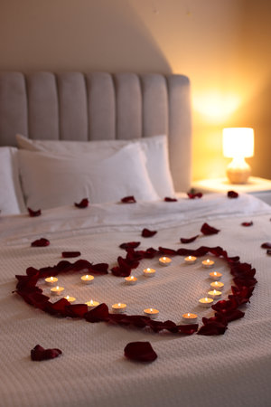 Heart made with beautiful rose petals and burning candles on bed indoorsの写真素材