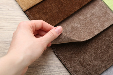 Woman with samples of different fabrics at wooden table, closeup