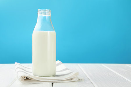 Fresh milk in glass bottle on white wooden table against light blue background. Space for textの写真素材