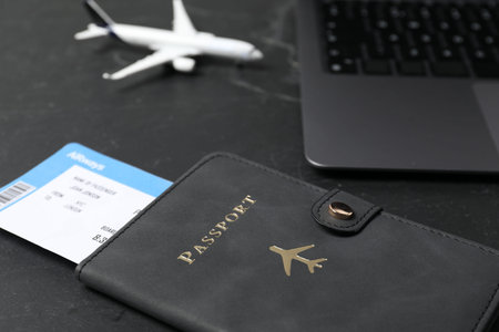 Passport, flight ticket, plane model and laptop on black table, closeup