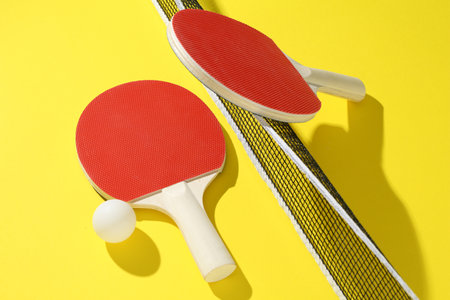 Ping pong rackets, ball and net on yellow backgroundの写真素材