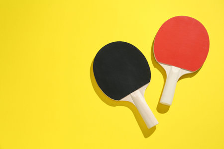 Ping pong rackets on yellow background, top view. Space for text
