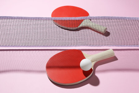 Ping pong rackets, ball and net on pink background, above view