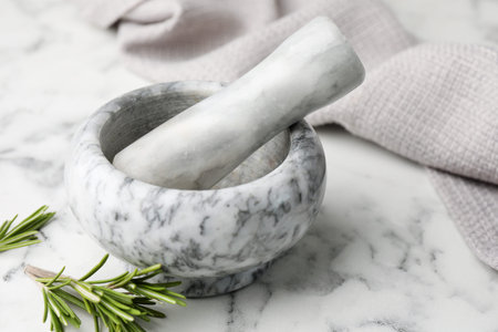 Mortar with rosemary, pestle and cloth on white marble table, closeupの写真素材