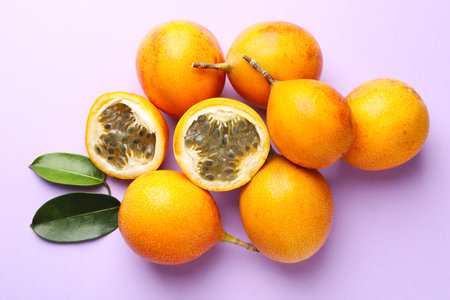 Ripe yellow passion fruits and leaves on lilac background, flat lay
