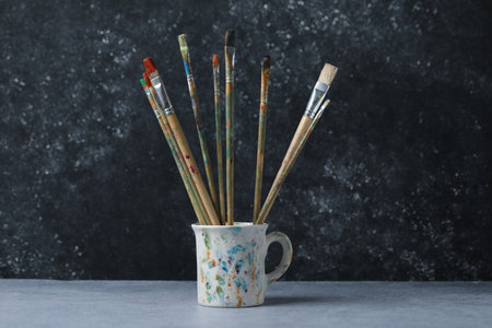 Dirty paintbrushes in cup on grey tableの写真素材