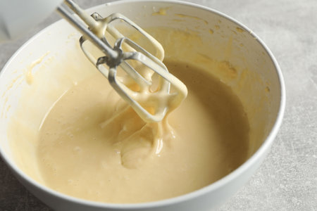 Hand mixer with whisks and bowl of dough on grey textured table, closeupの写真素材