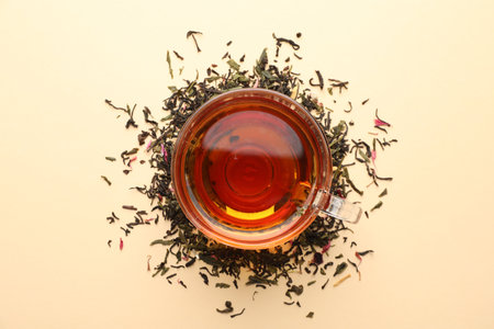 Delicious herbal tea in glass cup and dry leaves on beige background, flat layの写真素材
