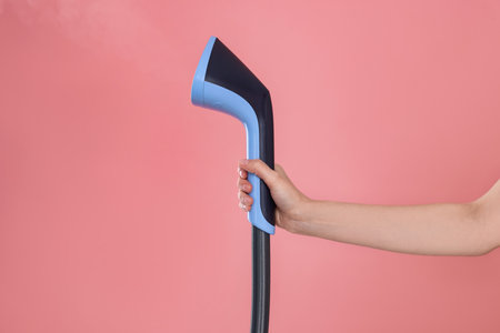 Woman with clothes steamer on pink background, closeupの写真素材