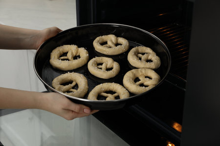 Woman putting baking dish with uncooked pretzels into oven, closeupの写真素材