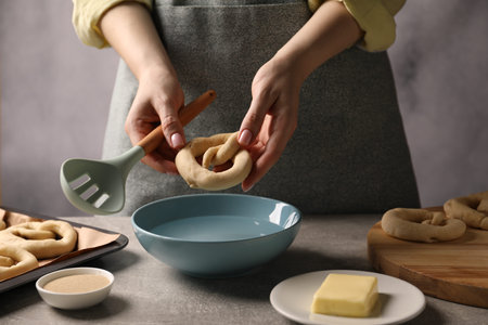 Woman putting uncooked pretzel into bowl of water at grey table, closeupの写真素材