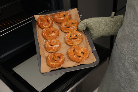 Woman taking baking dish with fresh pretzels out of oven, closeupの写真素材