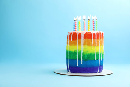Rainbow birthday cake with candles on light blue background, space for textの写真素材