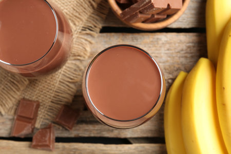 Tasty chocolate milk in glasses, pieces and bananas on wooden table, flat layの写真素材