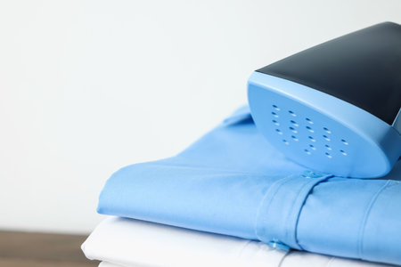 Upright steamer and stack of folded shirts on blurred background, closeup. Space for textの写真素材
